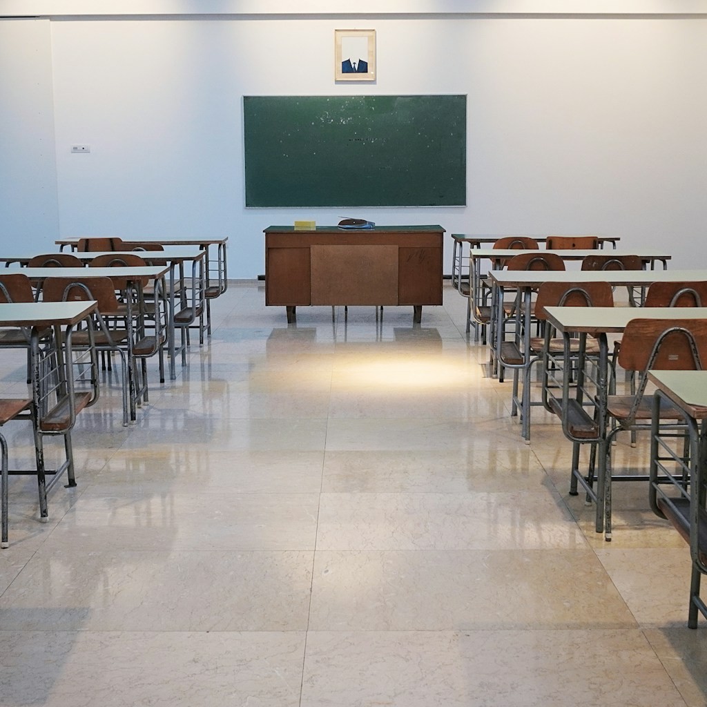 An empty high school science classroom with an anatomy model on the front desk and exam papers stacked beside it